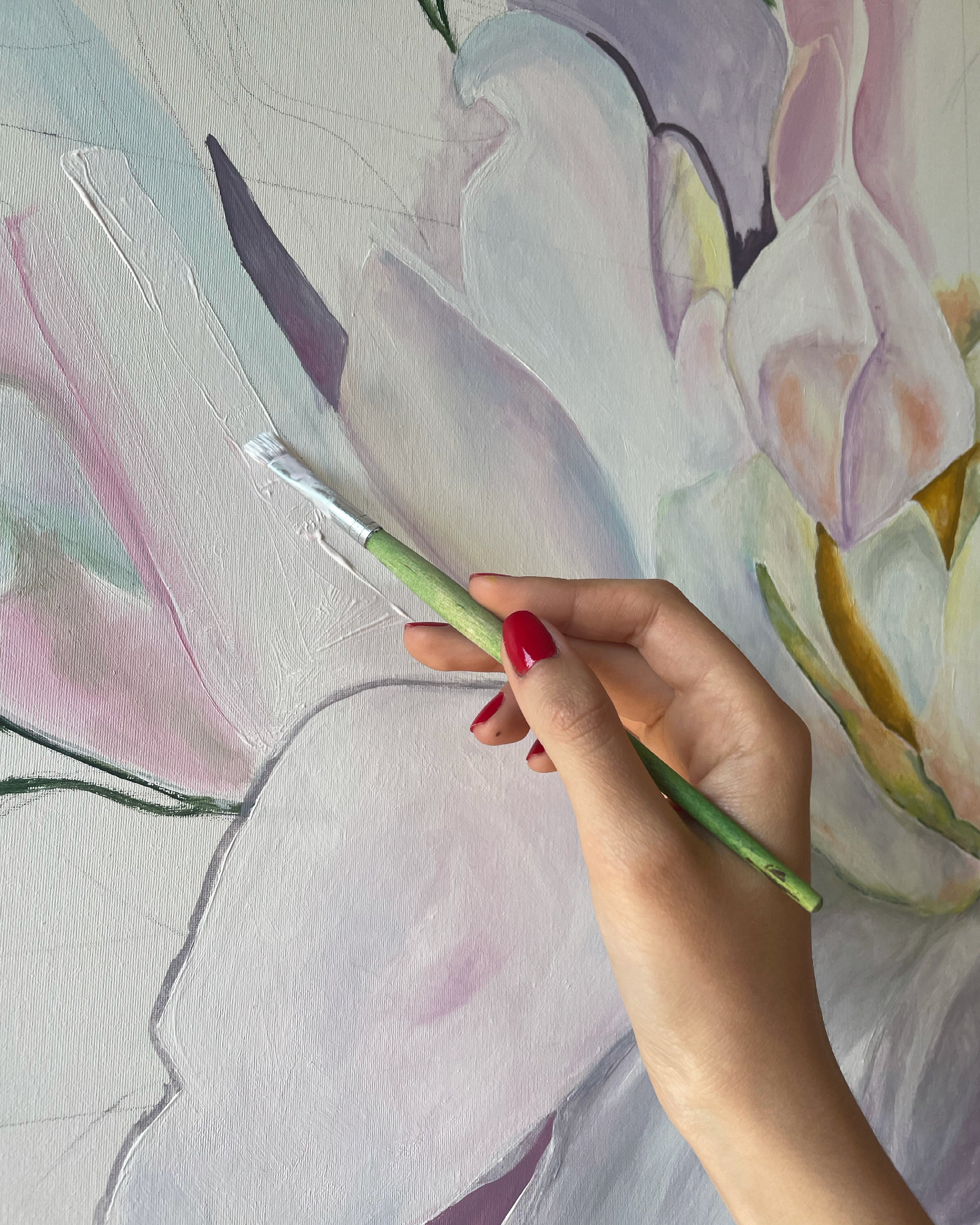 Hand holding a paintbrush over a floral painting with soft pastel colors.