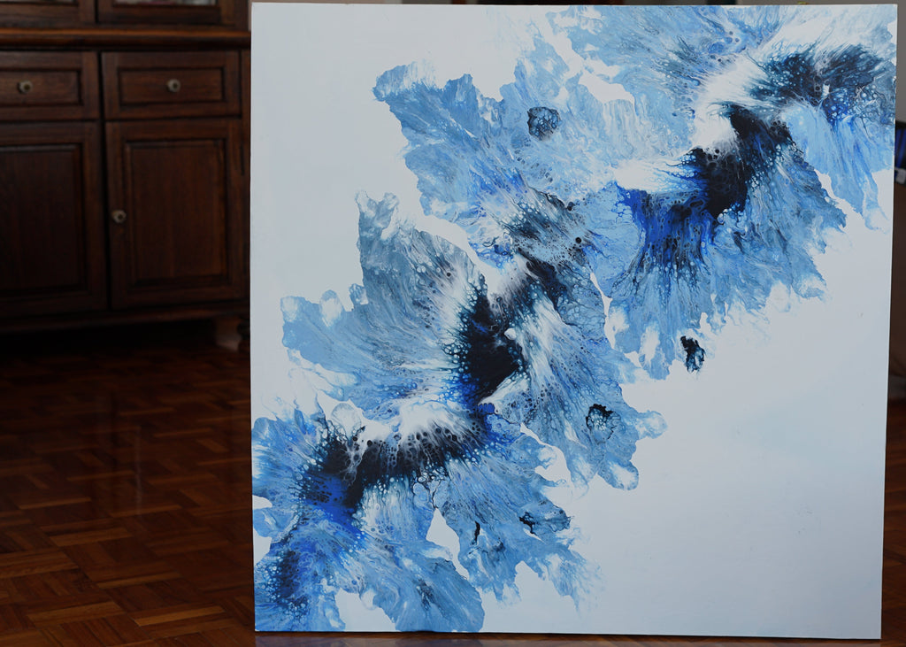 Abstract blue and black painting on a white canvas in a room with wooden flooring and furniture.