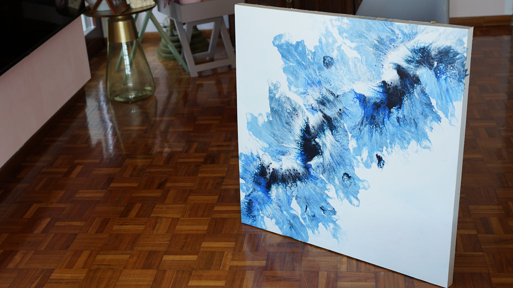 Abstract blue and black painting on a white canvas against a wooden floor background