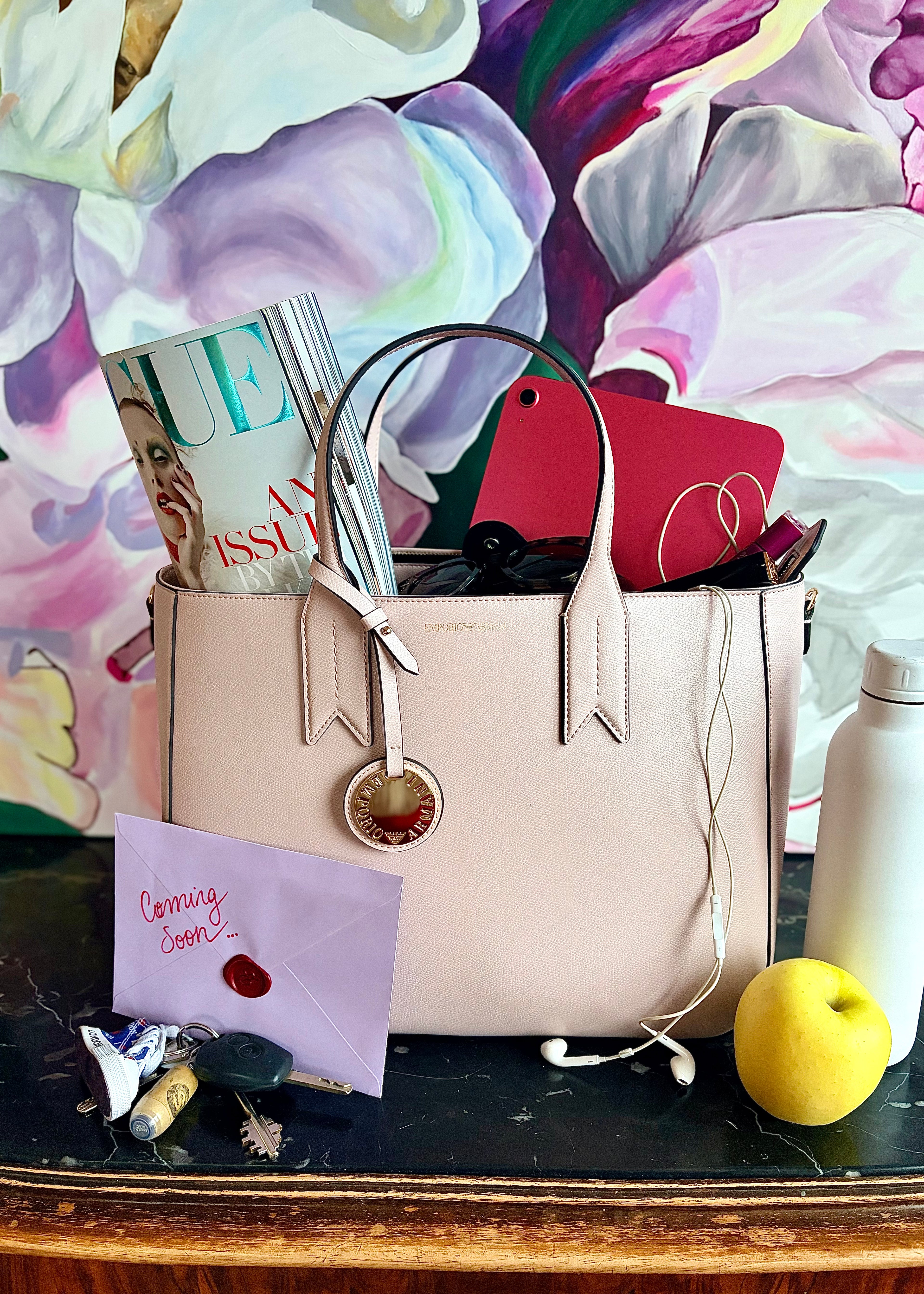 Beige handbag with items on a table against a colorful floral background